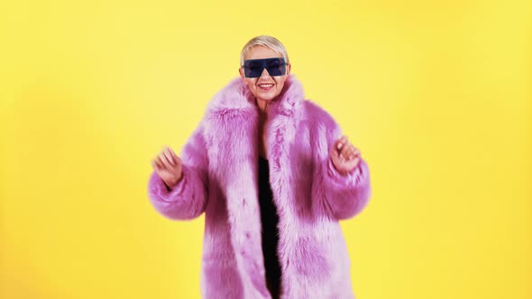 Woman in pink fur coat and sunglasses singing and dancing happily