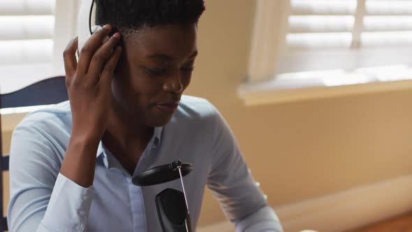 African american woman wearing headphones singing in microphone at home