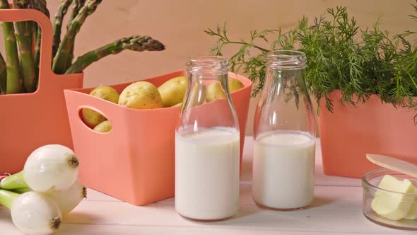 Spring Young Vegetables in Coral Containers and Bottles with Milk on Table