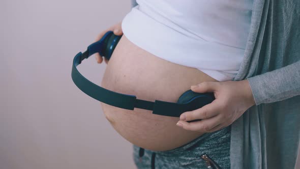 Pregnant Lady with Headphones on Tummy Dances at Light Wall