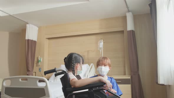 Asian scrub uniform nurse taking care of girl kid patient sitting on wheelchair in hospital ward.