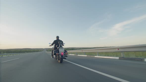 Man in black vest and helmet rides motorcycle on the highway and moves little away from the camera