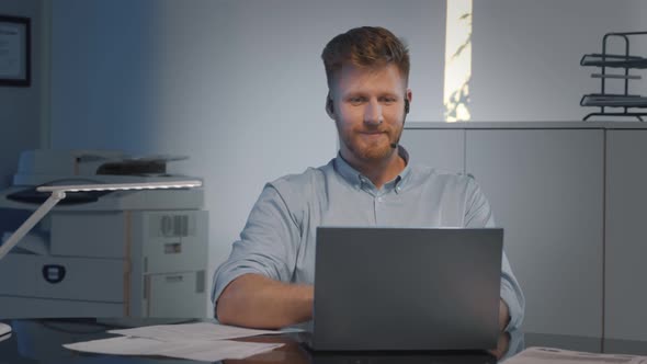 Handsome Male Call Center Operator in Headset Working with Laptop in Modern Office