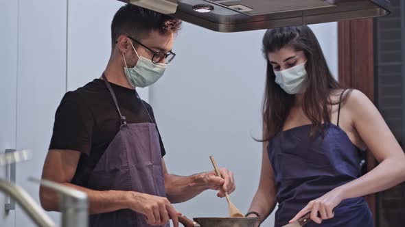 Two chefs in protective masks prepare food in the kitchen of a restaurant or hotel.