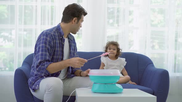 Hand father rolling cotton candy in candy floss machine and eat cotton candy together with daughter 