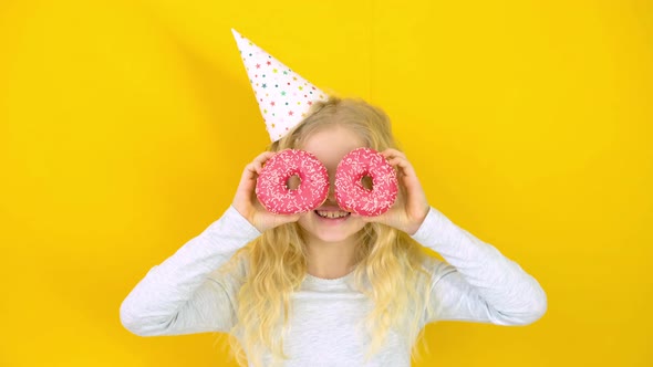 Crazy Cheerful Blonde Girl in Birthday Hat Smiling Having Fun and Looking Through Two Red Donuts on