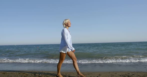 Blond Lady in White Summer Dressing Walks Along Sandy Beach