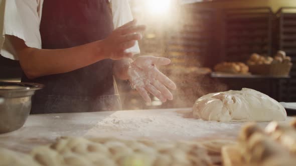 Animation of midsection of biracial male baker clapping hands to clean flour at bakery