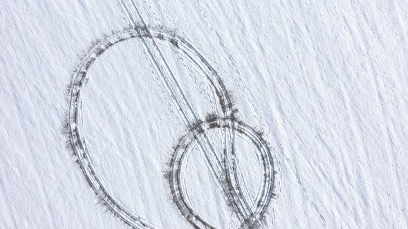 Ascending over the hill with circular vehicle tracks in the snow 4K drone video