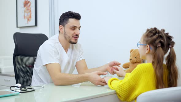 Middle Shot of Joyful Male Pediatrician Holding Hands of Patient Talking and Smiling