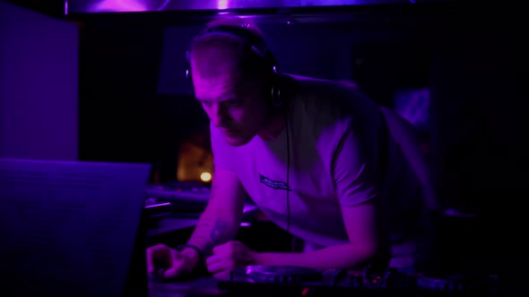 DJ in club working indoors in neon light. Caucasian male deejay person in nightclub using headphones