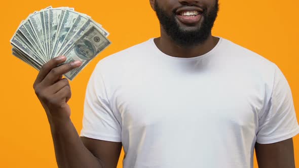 Rich Afro-American Male Holding Dollars on Yellow Background, Pointing by Hand