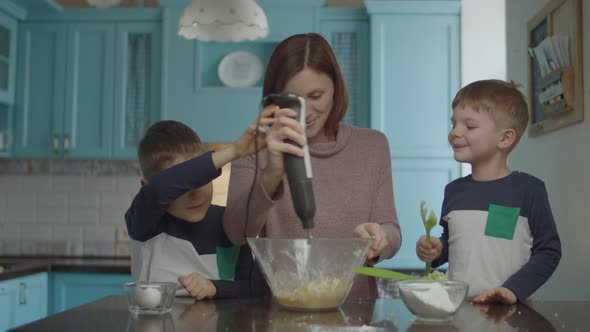 Kids helping mother to knead the dough with blender