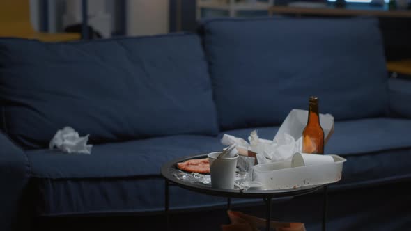 Chaos in Empty Living Room with Food Leftover and Bottle of Beer on Table