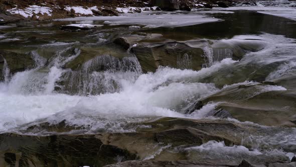 Rapid Flow of Water From a Mountain Creek and Stone Rapids with Snow in Winter. Waterfall