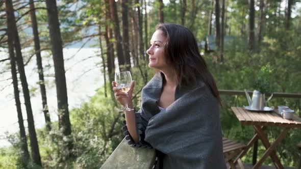 Beautiful Girl Wrapped in a Plaid on a Balcony in a Mountain House Enjoying a Glass of Wine