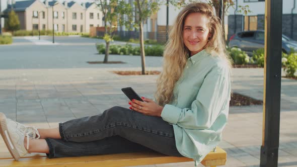 Portrait of Smiling Woman Sitting on Swing and Holding Smartphone