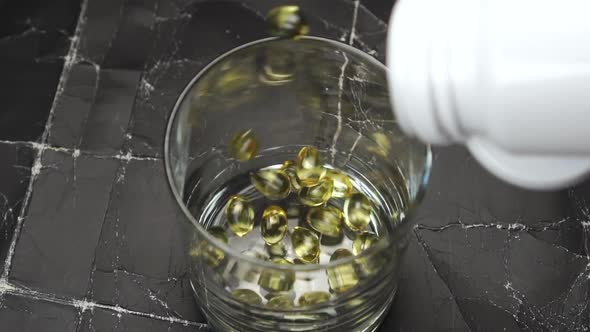 Omega 3 capsules fall into a glass from a white plastic bottle 