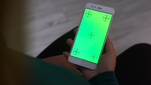 Woman at Home Using Smartphone with Green Mock-up Screen. 