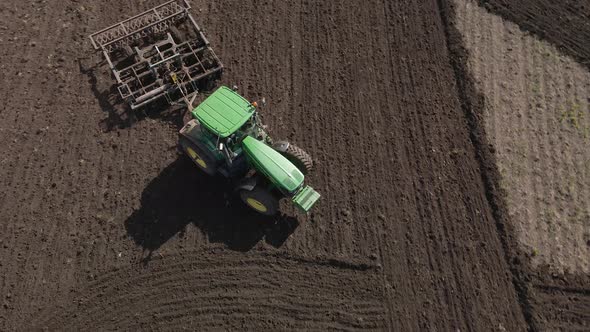 Agricultural green big tractor in the field plows with a plow