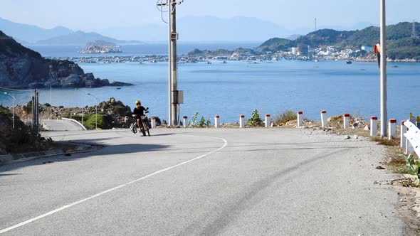 Driving a motorcycle on a road in Vietnam near sea, kitesurfing surfboard is attached to the bikes s