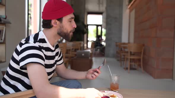 Man with a beard in a red hat enjoys his breakfast in a cozy cafe.