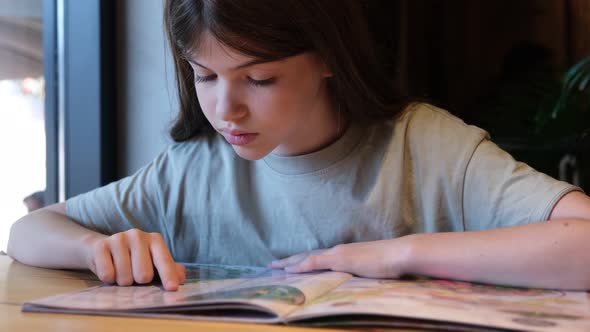 Little Young Girl Teenager Reads the Menu in a Cafe