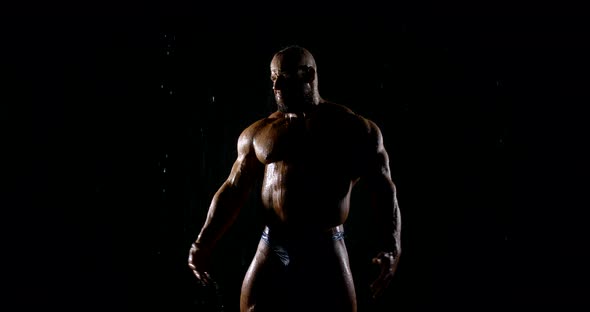 Brutal Muscular Bald Bearded Male Bodybuilder Close-up on a Black Background, He Poses, Shows Biceps