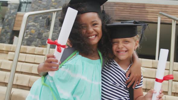 Video of happy diverse girls wearing graduation hats and holding diplomas