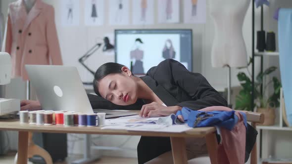 Asian Female Designer In Business Suit With A Laptop Sleeping While Designing Clothes In The Studio
