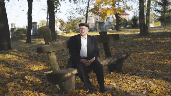 Senior Man in Cap Resting on a Park Bench and Telling When Leans Hand on Wood