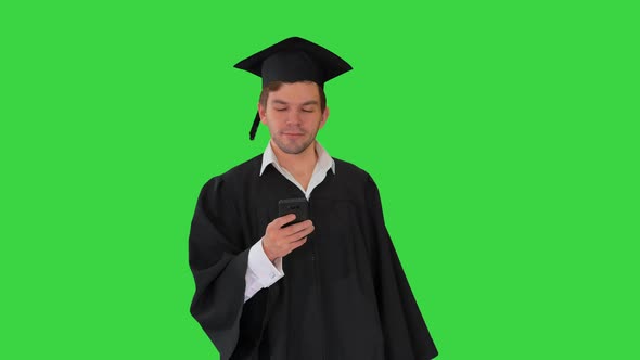 Male Student in Graduation Gown Checking His Phone While Walking on a Green Screen Chroma Key