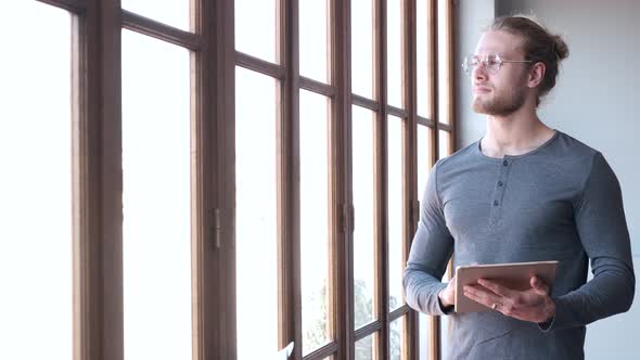 Man holds a digital tablet and looks out of the window