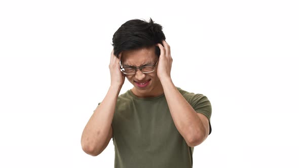 Portrait of Exhausted Asian Man 20s Wearing Glasses Frowning and Rubbing Temples in Headache