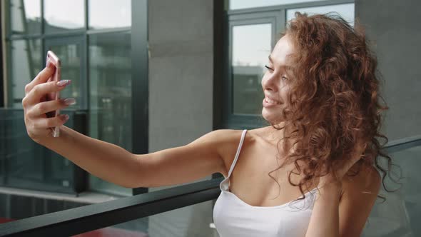 A Young Woman is Standing on the Balcony and Taking a Selfie