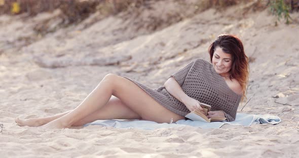 Beautiful brunette woman laughs and smiles while using her mobile phone device laying on the beach o
