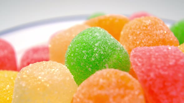 Multicolored marmalade candy with sugar in white plate. Gelatin sweet snack. Macro