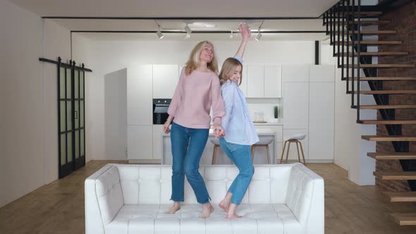 Happy Family Senior Mom Having Fun with Adult Daughter Dancing on Sofa in Living Room