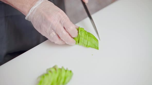 Hands of Male Cook Cutting Fresh Avocado on Board in Restaurant Kitchen