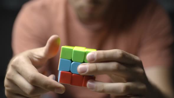 Close-up from front of young male hands solving colorful Rubik’s cube