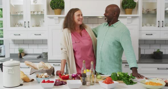 Animation of happy diverse female and male senior friends preparing meal in kitchen, embracing