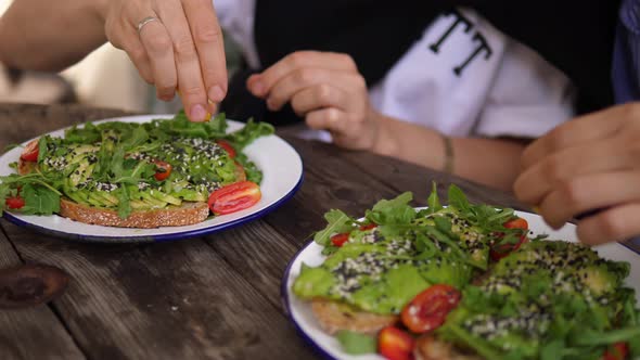 Two Friends Dress Avocado Toasts with Lemon Juice in Cafe