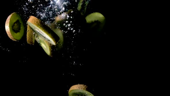 Kiwis dropped into water on black background, side lit slow motion