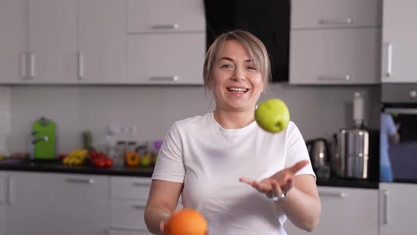 Cheerful Woman Juggling Fruits in Domestic Kitchen