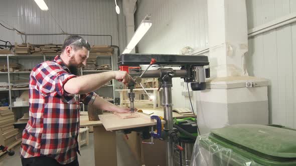 Man Carpenter in a Shirt Using Drilling Machine in Workshop