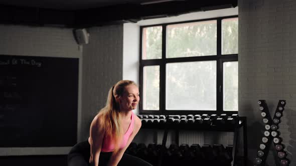 Attractive young beautiful woman doing cardio exercise and squatting with kettlebell in gym