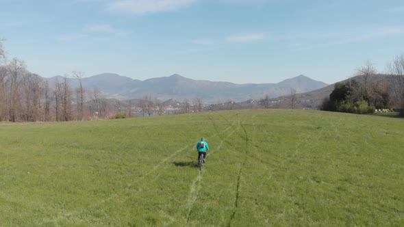 Aerial: man having fun by riding mountain bike in the grass on sunny day, scenic alpine landscape,