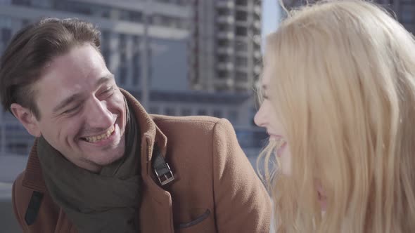 Portrait of Handsome Man and Pretty Blond Woman in Warm Jacket Sitting at the City Street Talking