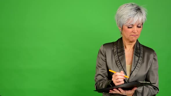 Business Middle Aged Woman Writes To Paper and Smiles To Camera - Green Screen - Studio