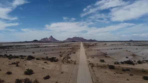 Three cars are driving on a long dusty road of the desert, Namibia, aerial shot